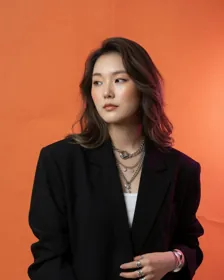오렌지 배경 앞에서 옆을 보는 검은 재킷 차림의 사람